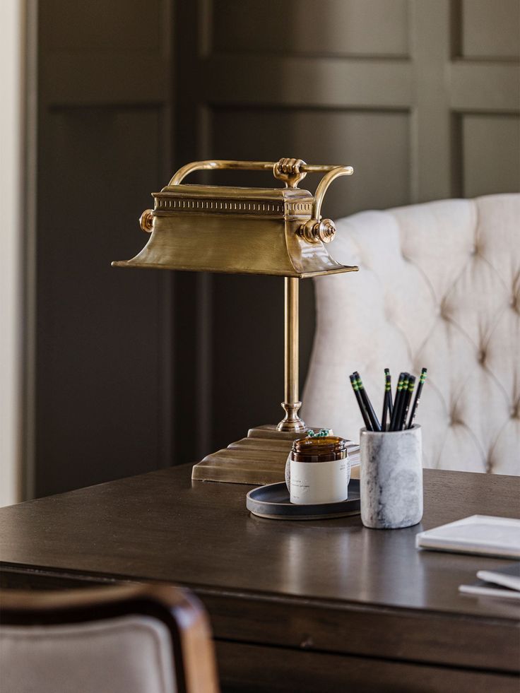 a desk lamp sitting on top of a wooden table next to a cup and pen holder