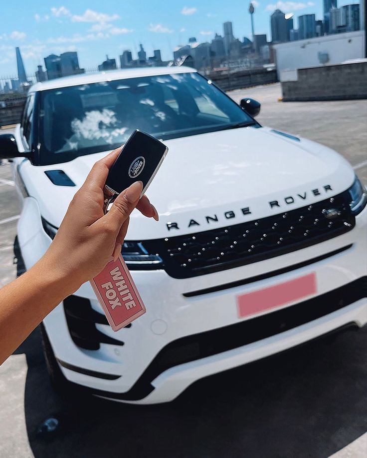 a person holding up a cell phone in front of a white car with the name range rover on it