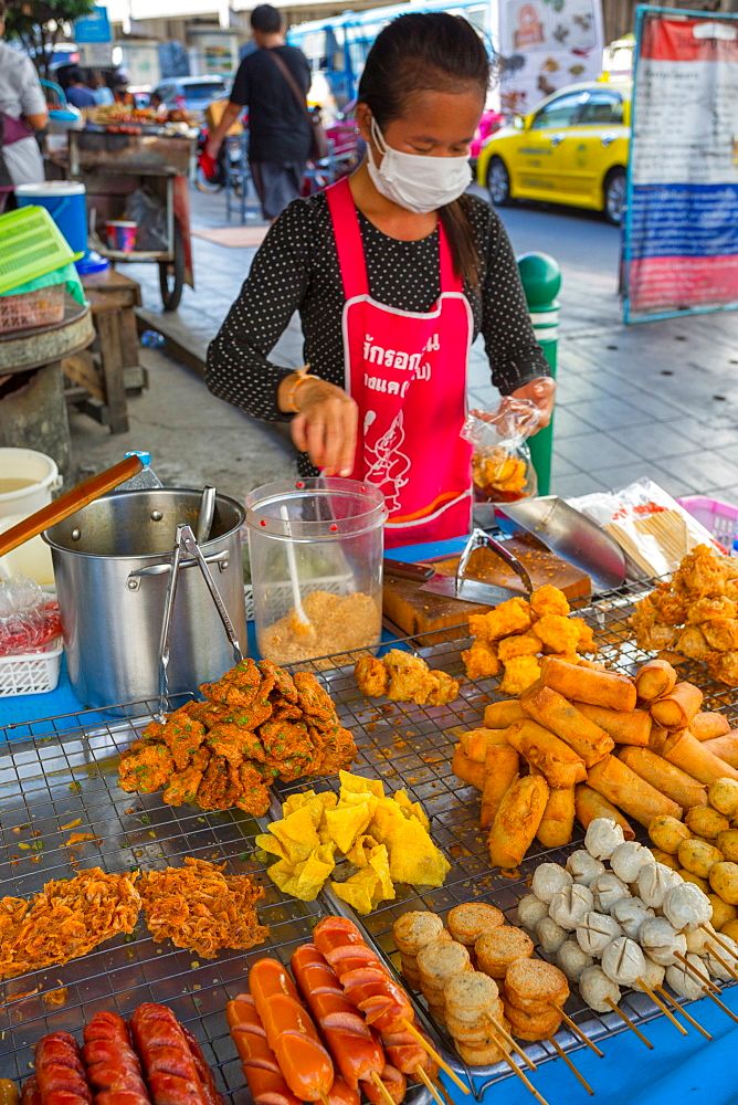 a woman wearing a face mask standing in front of a table filled with different types of food