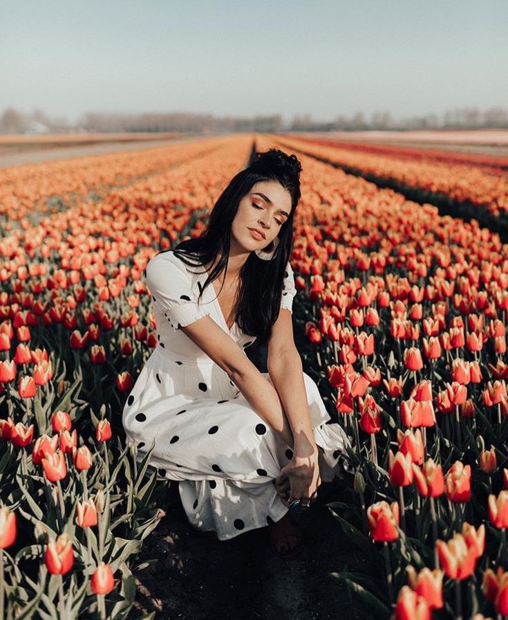 a woman kneeling in a field full of red tulips with her hands on her knees