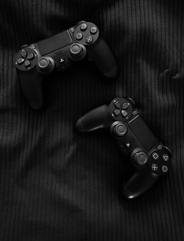 two video game controllers sitting next to each other on a black cloth covered bed sheet