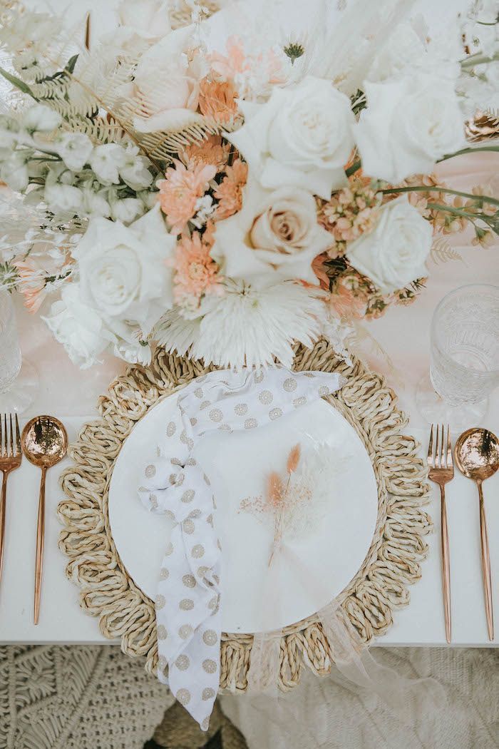 a table setting with white flowers and gold place settings on top of the table, along with silverware