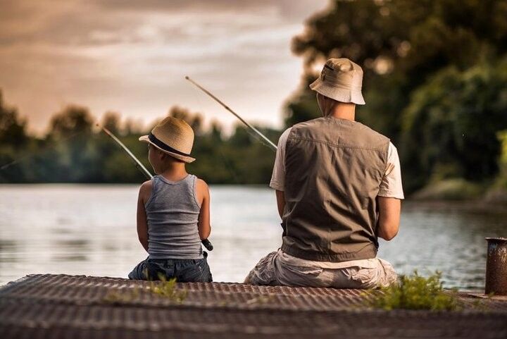 an older man and young boy sitting on a dock fishing