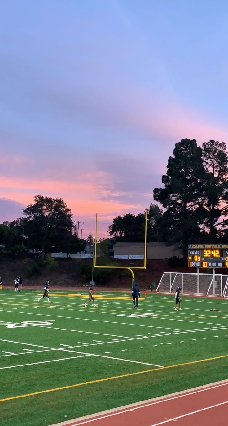 a group of people playing soccer on a field at sunset with the sky in the background