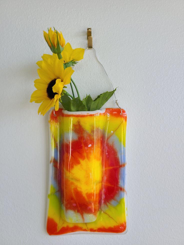 a vase with flowers in it hanging on the wall next to a hook that is attached to a wall