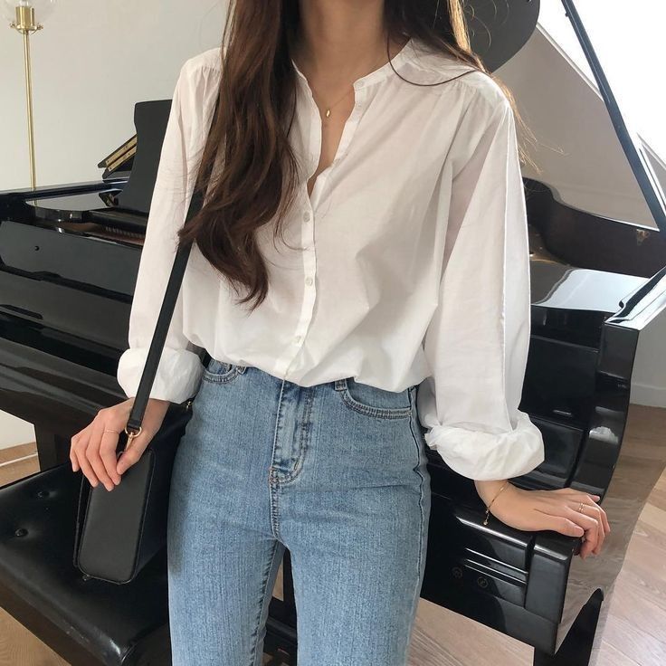 a woman standing in front of a piano with her hands on her hips, wearing jeans and a white shirt