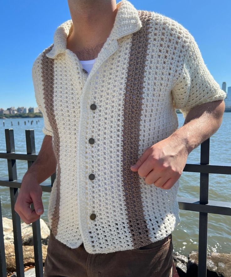 a man wearing a crochet jacket by the water