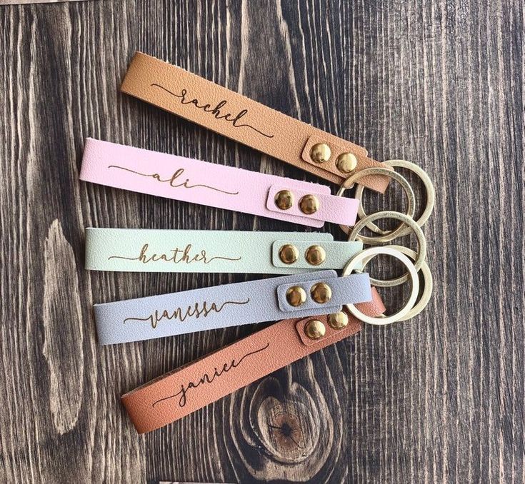 four personalized leather key fobrings with name tags on them sitting on top of a wooden table