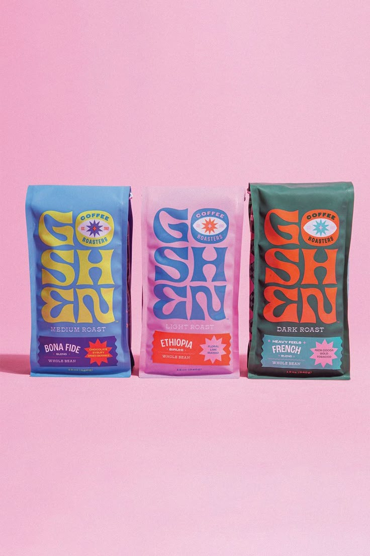 three bags of coffee sitting next to each other on a pink background with the same bag in different colors