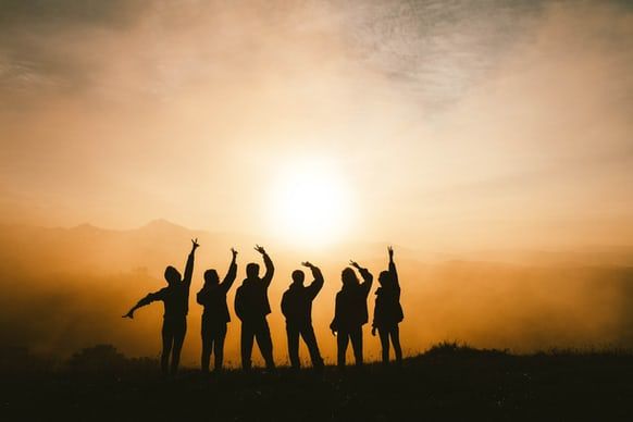 a group of people standing on top of a hill with their arms in the air