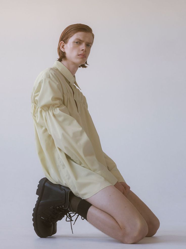 a woman sitting on the ground with her legs crossed wearing black boots and a yellow shirt