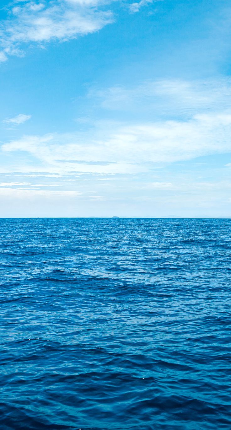 the ocean is blue and calm with some clouds in the sky