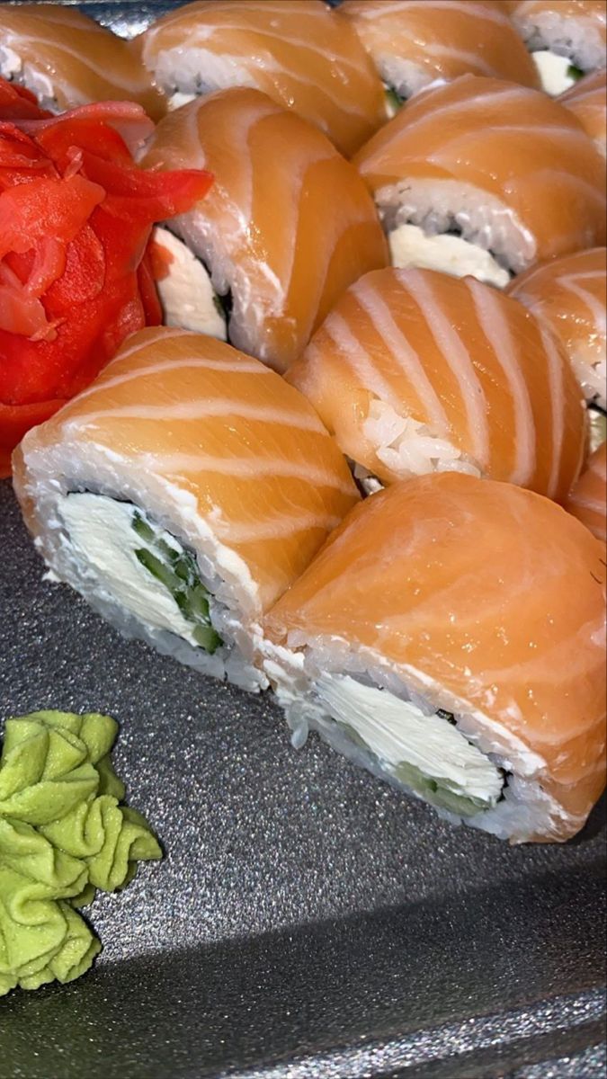 several sushi rolls are arranged on a tray next to a red pepper and tomato