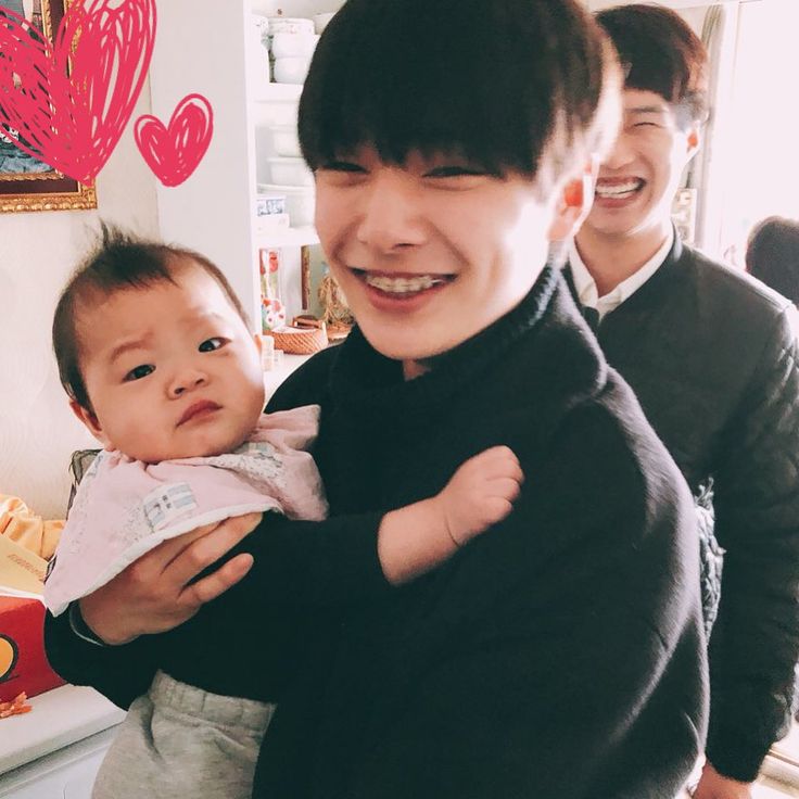 a man holding a baby in his arms and smiling at the camera with two other people behind him