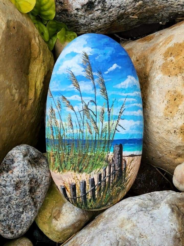 a painted rock sitting on top of rocks next to some grass and water in the background