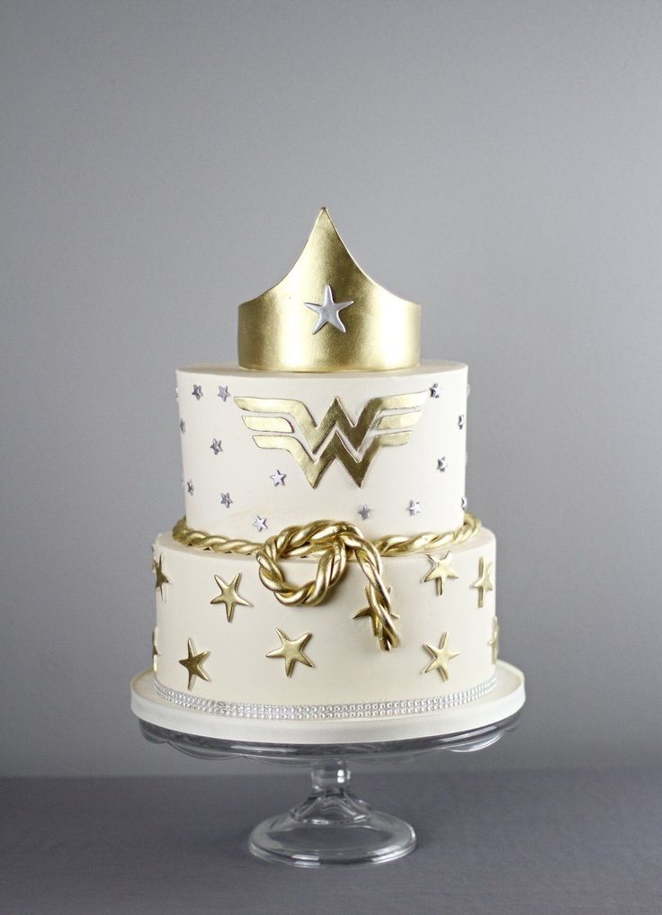 a three tiered cake with gold stars and a wonder woman crown on the top