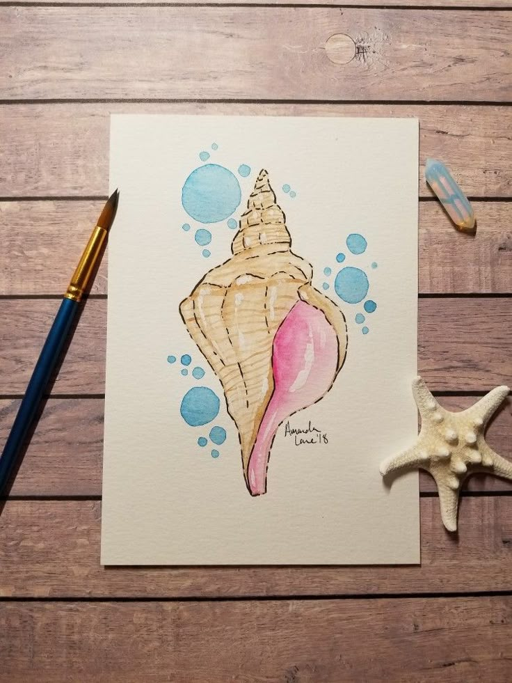 a watercolor painting of a seashell and starfish on a wooden table with paintbrushes