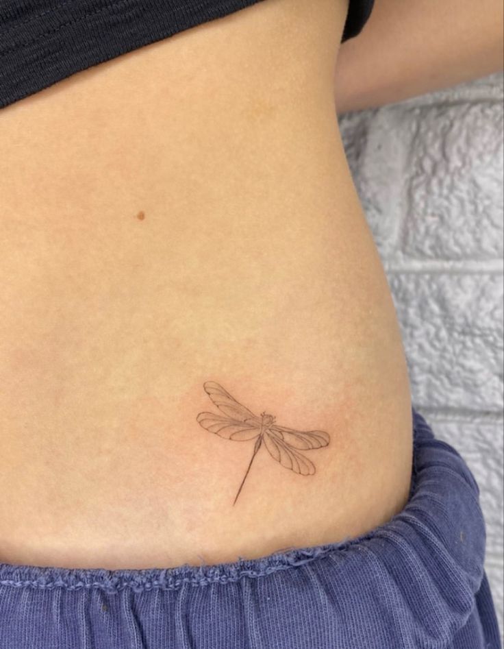 a woman's stomach with a small dragonfly tattoo on it