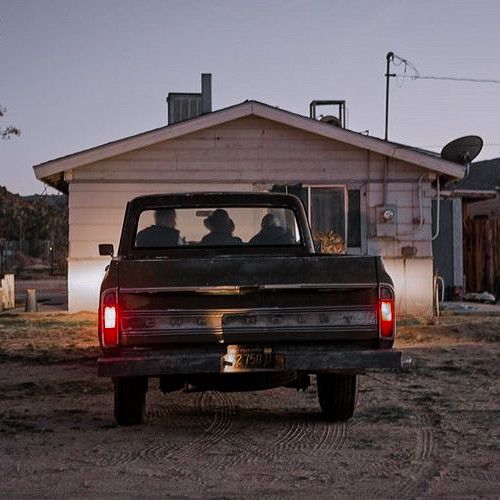 two people are sitting in the back of a pick - up truck at dusk,