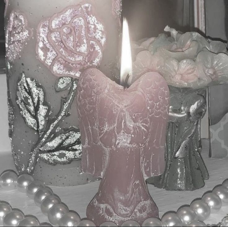 a pink candle sitting on top of a table next to pearls