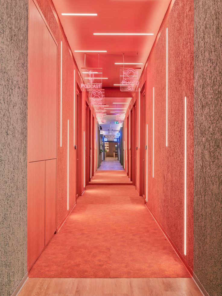 a long hallway with red walls and wooden floors is lit by neon lights on the ceiling