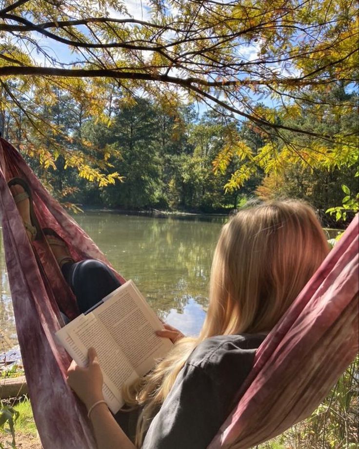 a woman sitting in a hammock reading a book