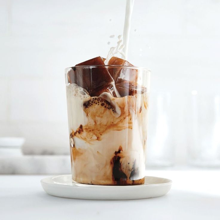 a glass filled with ice and milk on top of a white plate