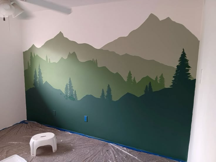 an empty room with mountains painted on the wall and paint rollers in front of it