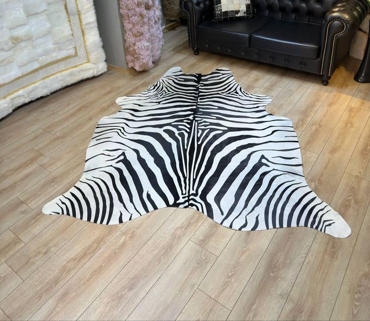 a zebra print rug is laying on the floor in front of a black leather couch