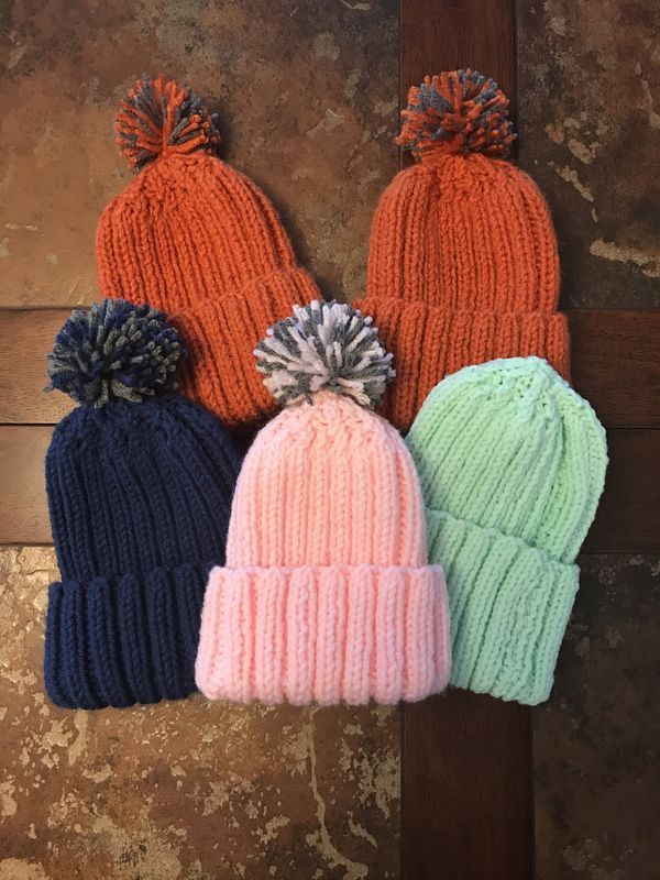 three knitted hats with pom poms hanging from the side on a wooden wall