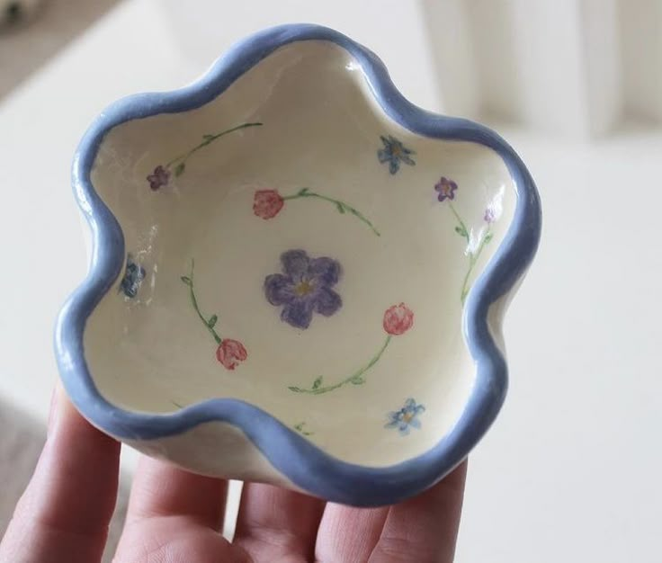 a hand holding a small bowl with flowers painted on the bottom and blue trim around the edge