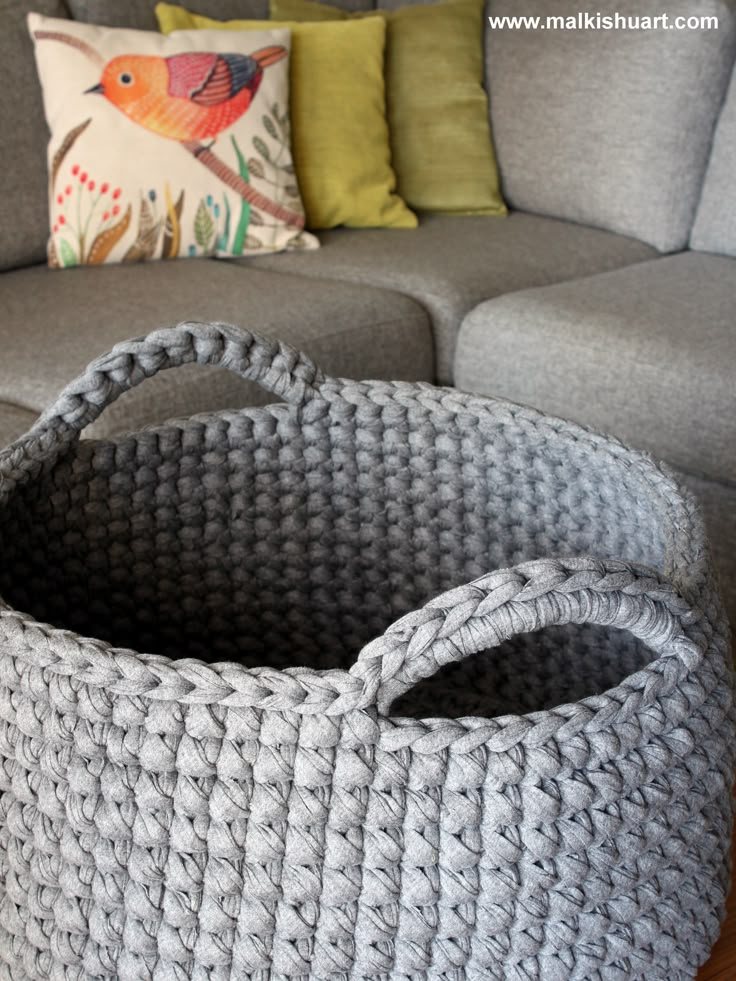 a large gray basket sitting on top of a wooden table next to a couch and pillows