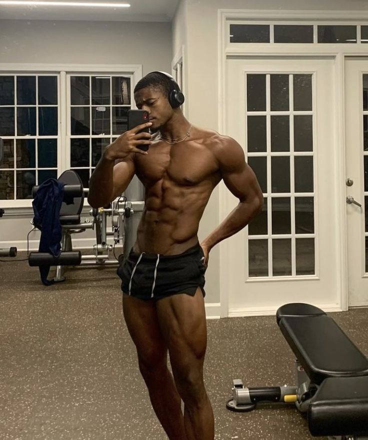 a shirtless man standing in front of a gym machine while talking on a cell phone