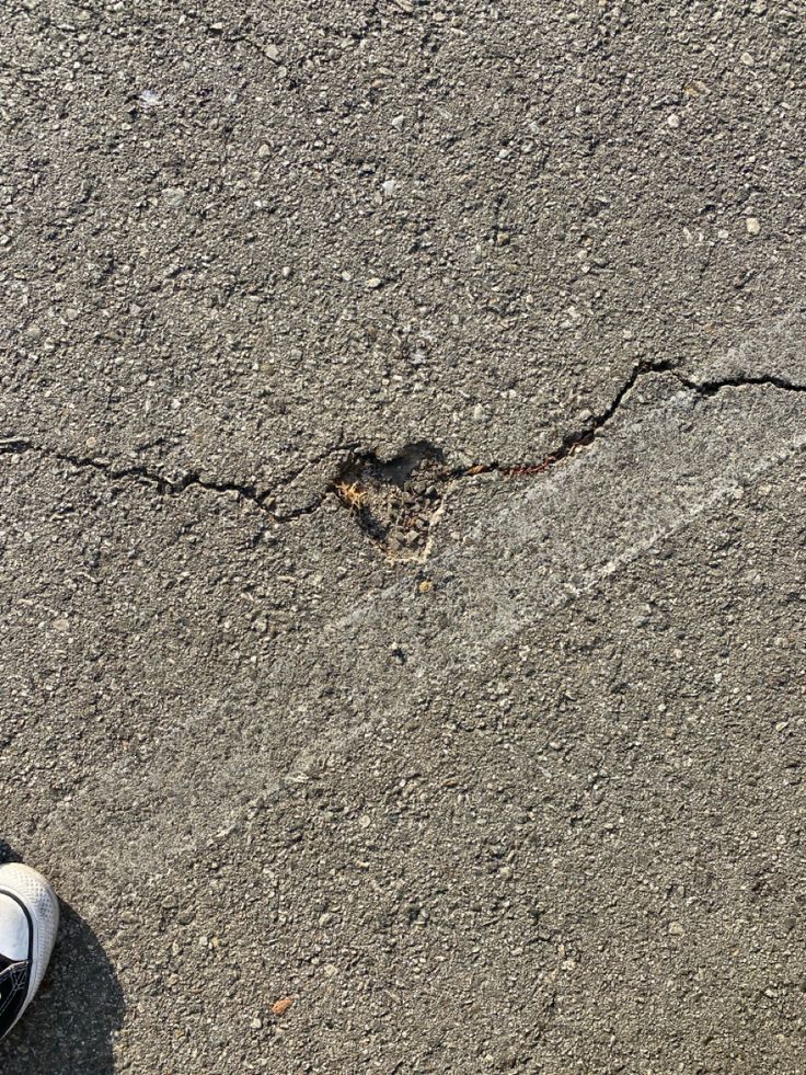 a person standing on the sidewalk with their feet in the air and cracked asphalt behind them