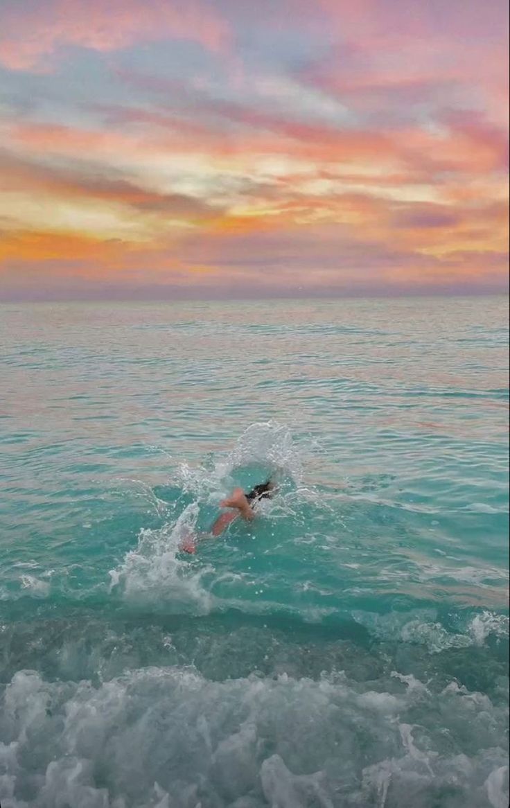 a person is swimming in the ocean at sunset or dawn with colorful clouds and blue water