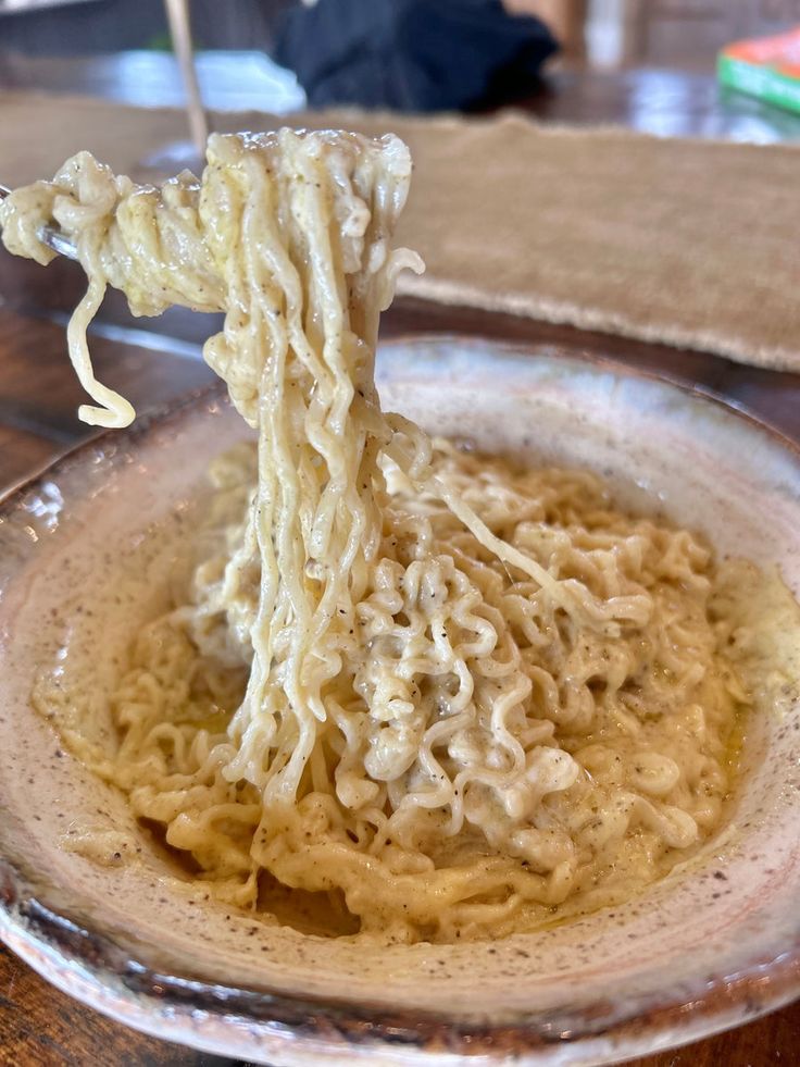 a bowl of noodles is being held up by a pair of chopsticks in it