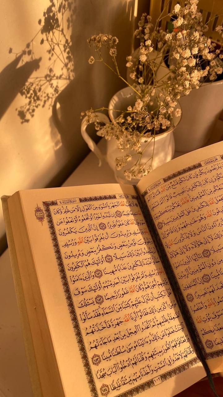 an open book sitting on top of a table next to a vase filled with flowers