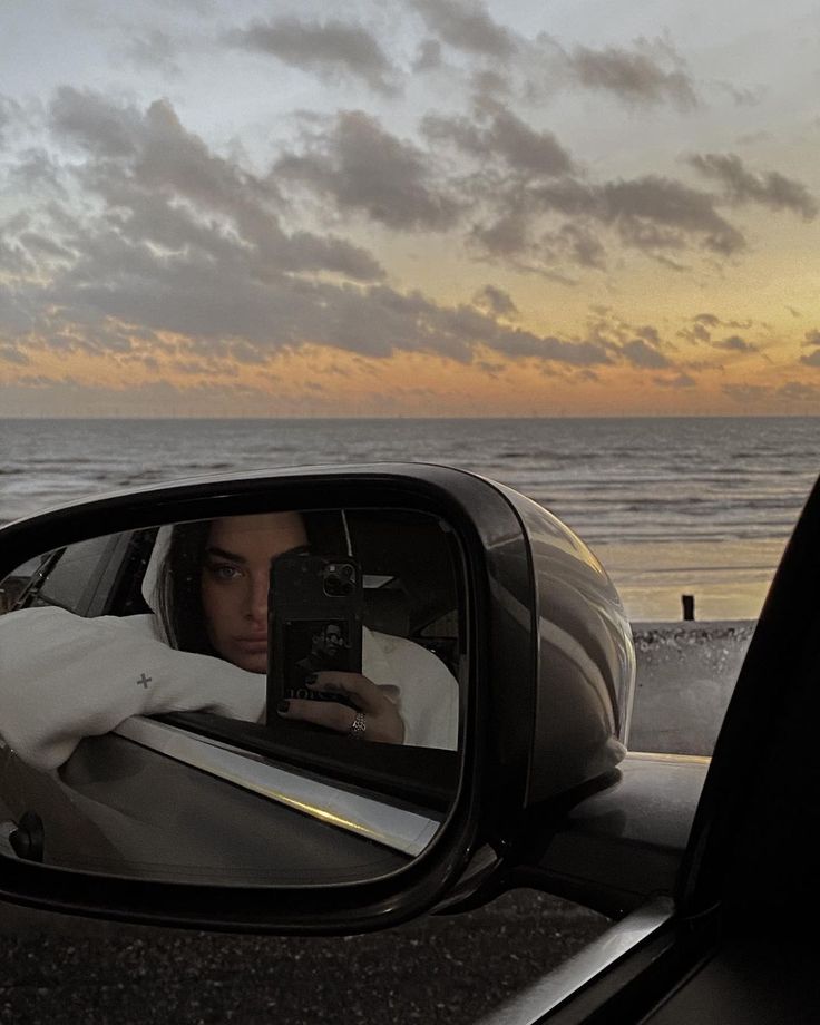 a man taking a photo in the side view mirror of a car near the ocean