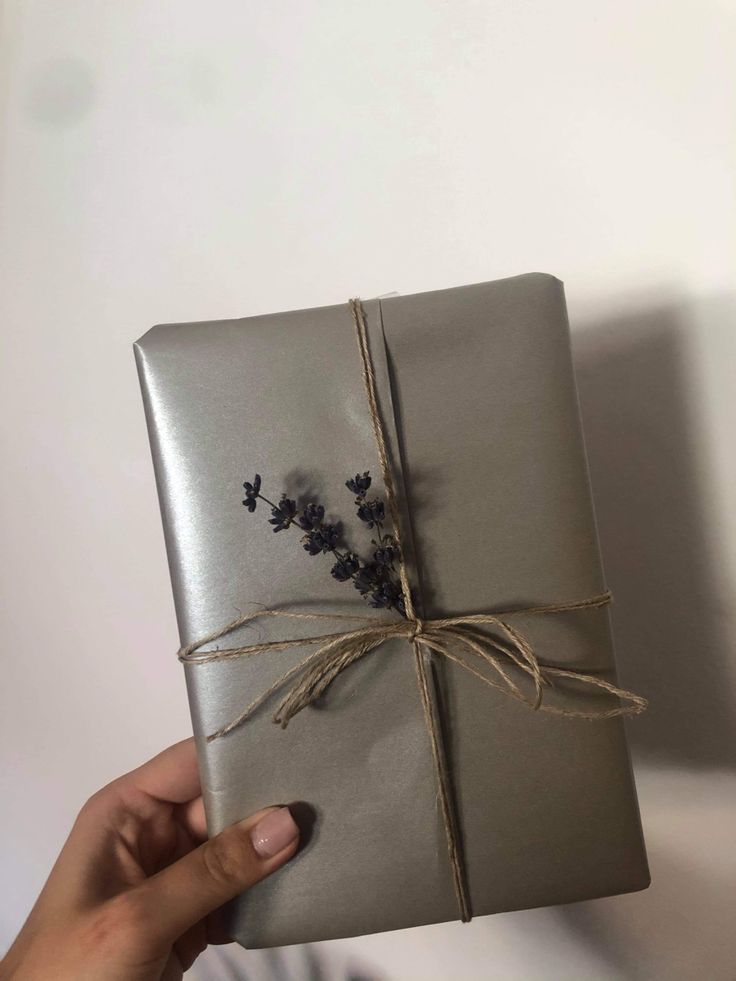 a person holding a wrapped present in silver paper with lavenders on the wrapper