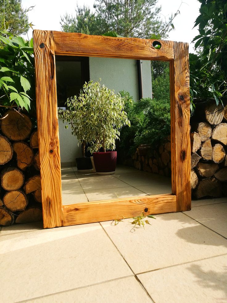 a mirror sitting on top of a stone floor next to a pile of logs and a potted plant