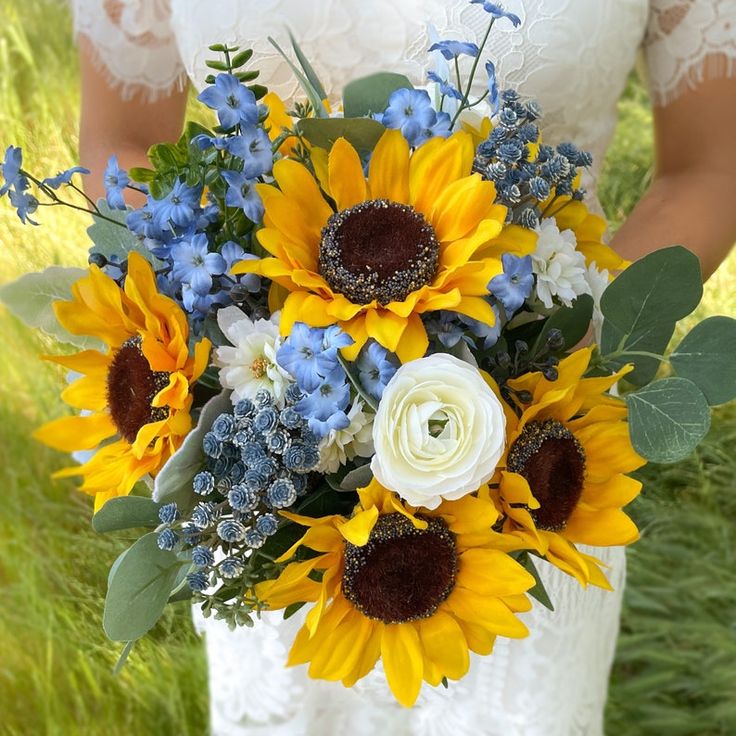 a bride holding a bouquet of sunflowers and blue flowers in her hands on the grass