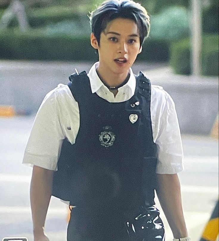 a young man walking down the street wearing a black vest