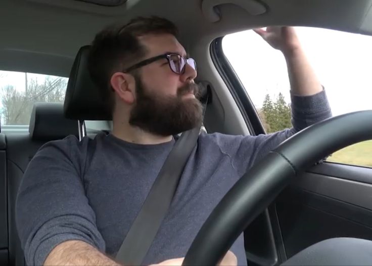 a man driving a car with his hand on the steering wheel while wearing sunglasses and looking off to the side