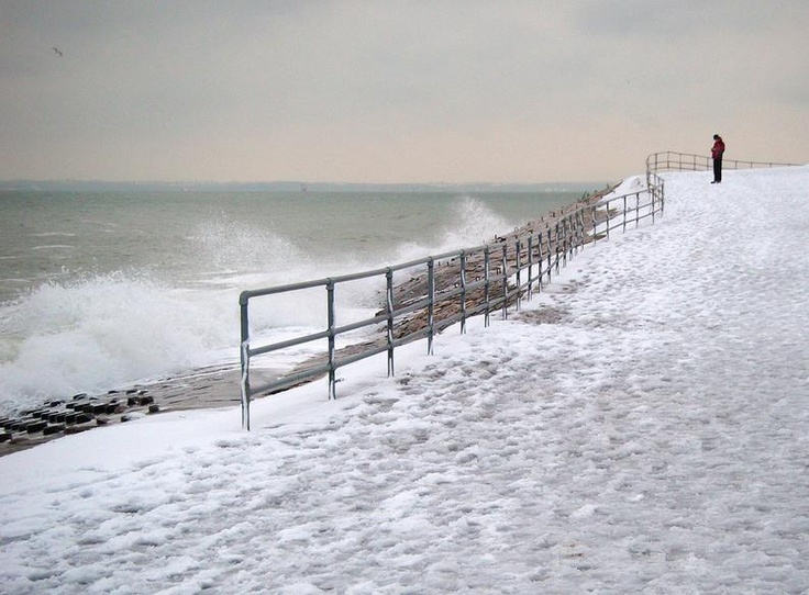 a man standing on top of a snow covered beach next to the ocean with waves crashing