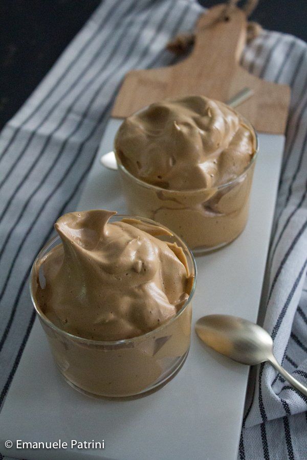 two bowls filled with peanut butter on top of a white cutting board next to a spoon