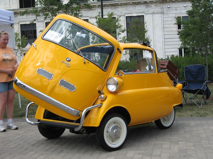 an old yellow car is parked in front of a building with people standing around it