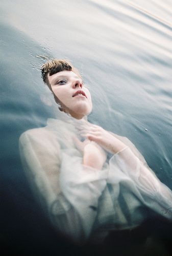 a woman floating in the water wearing a white dress