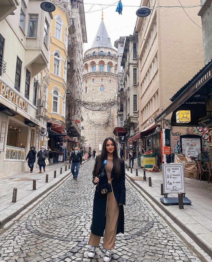 a woman standing in the middle of a cobblestone street next to tall buildings