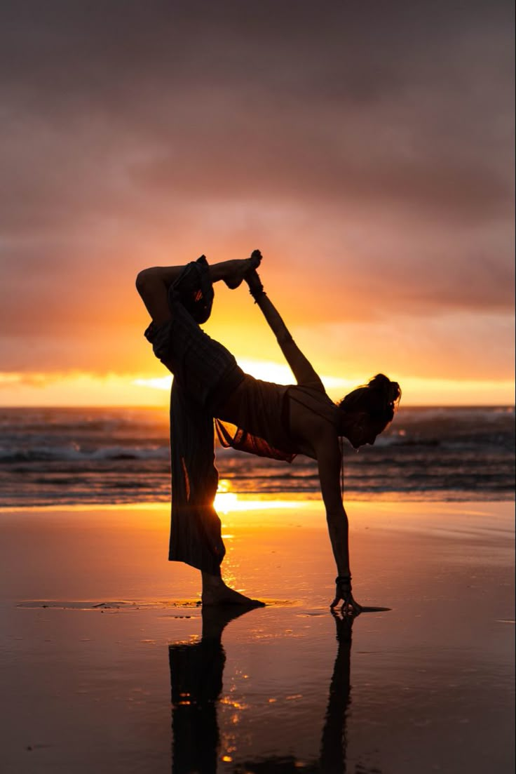 a woman doing yoga on the beach at sunset