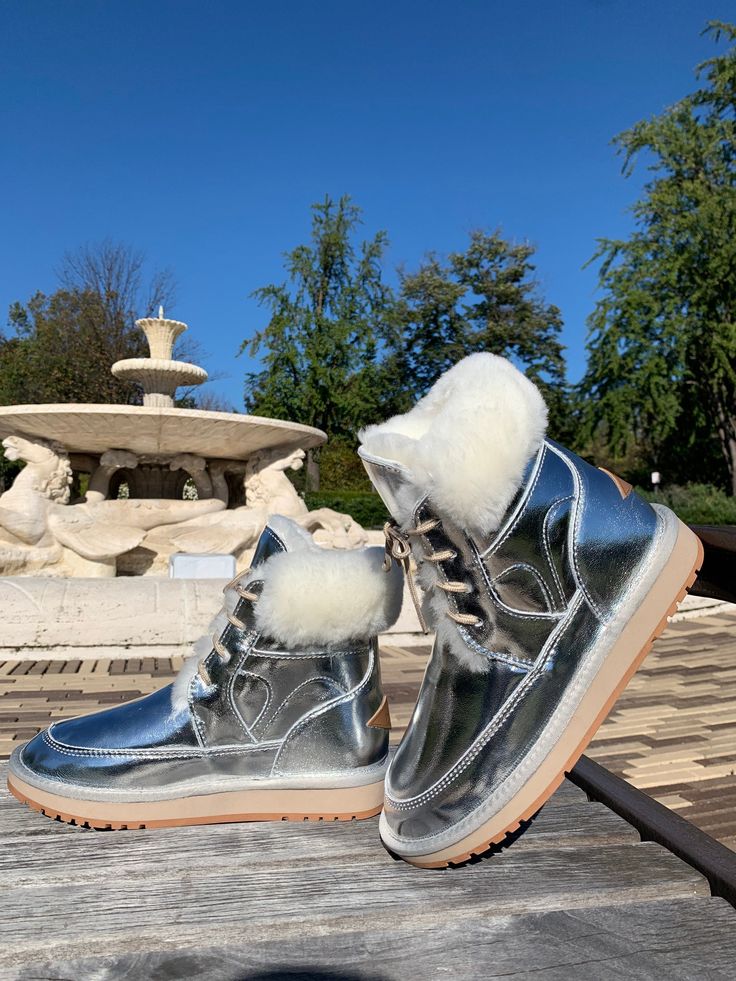 a pair of silver shoes sitting on top of a wooden table next to a fountain